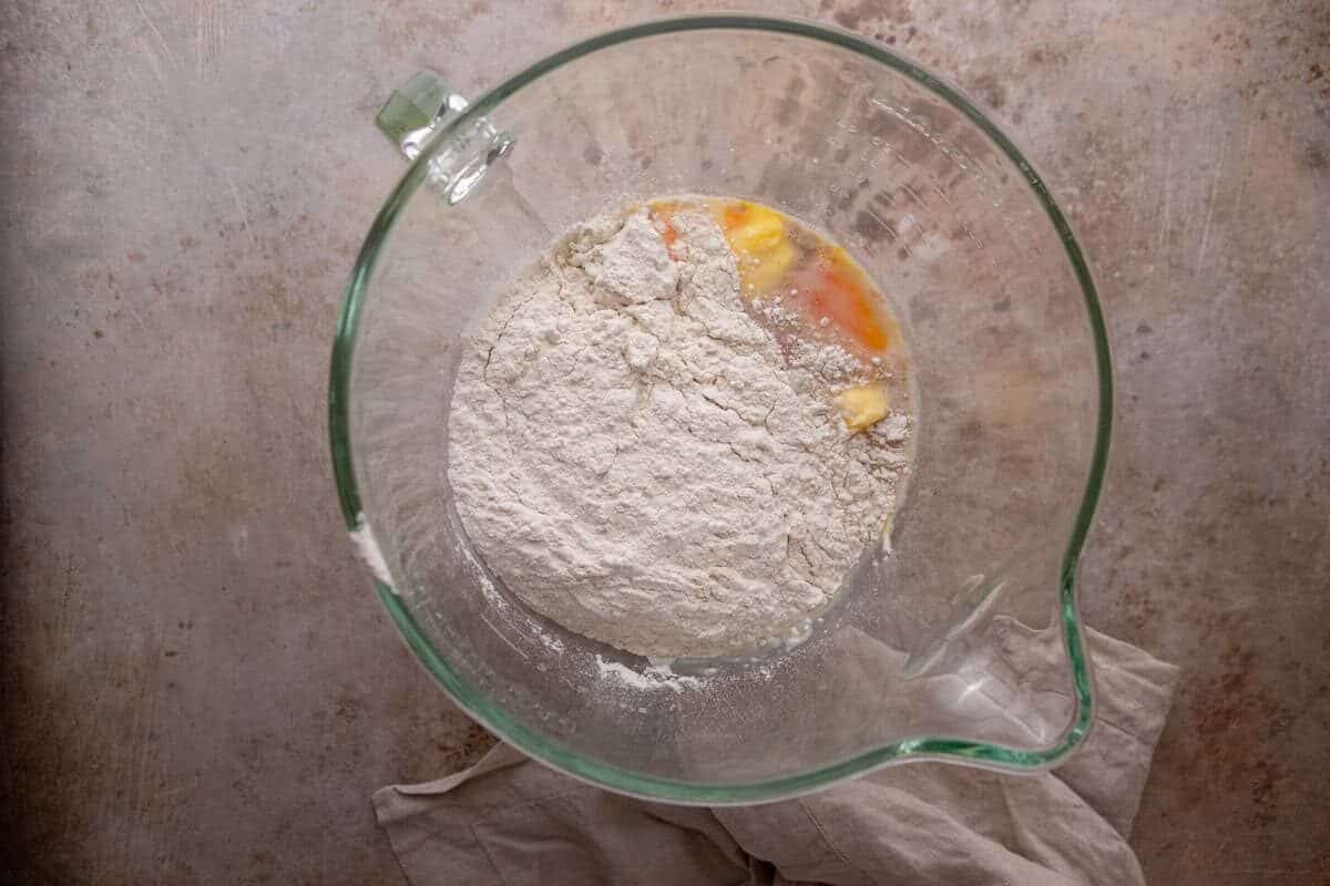 Flour, eggs, and melted butter in a glass mixing bowl for cinnamon roll dough