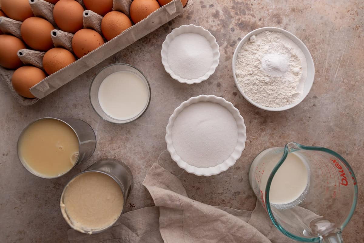 Tres leches cake ingredients including eggs, flour, sugar, milk, evaporated milk, and condensed milk