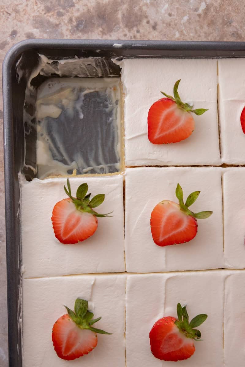 Tres leches cake cut into squares and topped with strawberries in the pan