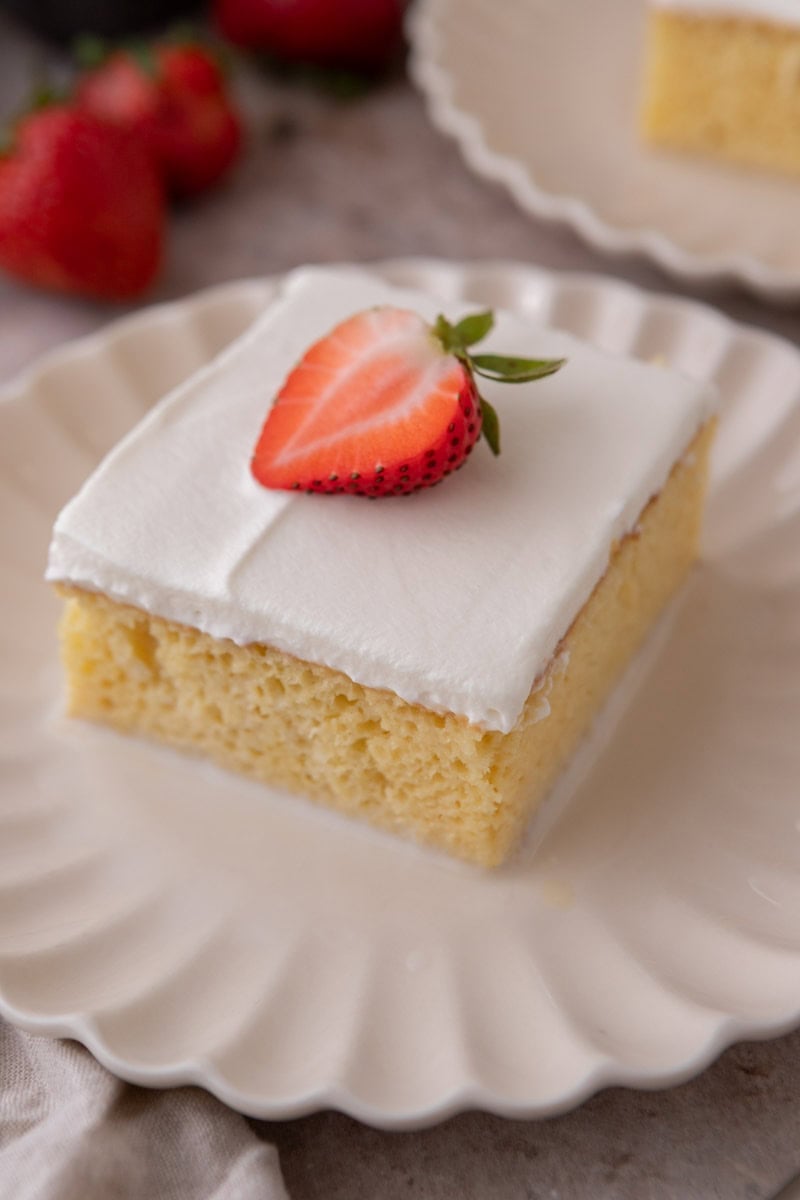Plated slice of tres leches cake topped with whipped cream and a fresh strawberry