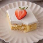 Plated tres leches cake square with a bite taken out, topped with a strawberry