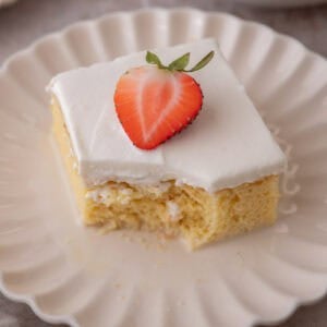 Plated tres leches cake square with a bite taken out, topped with a strawberry