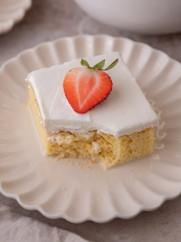 Plated tres leches cake square with a bite taken out, topped with a strawberry