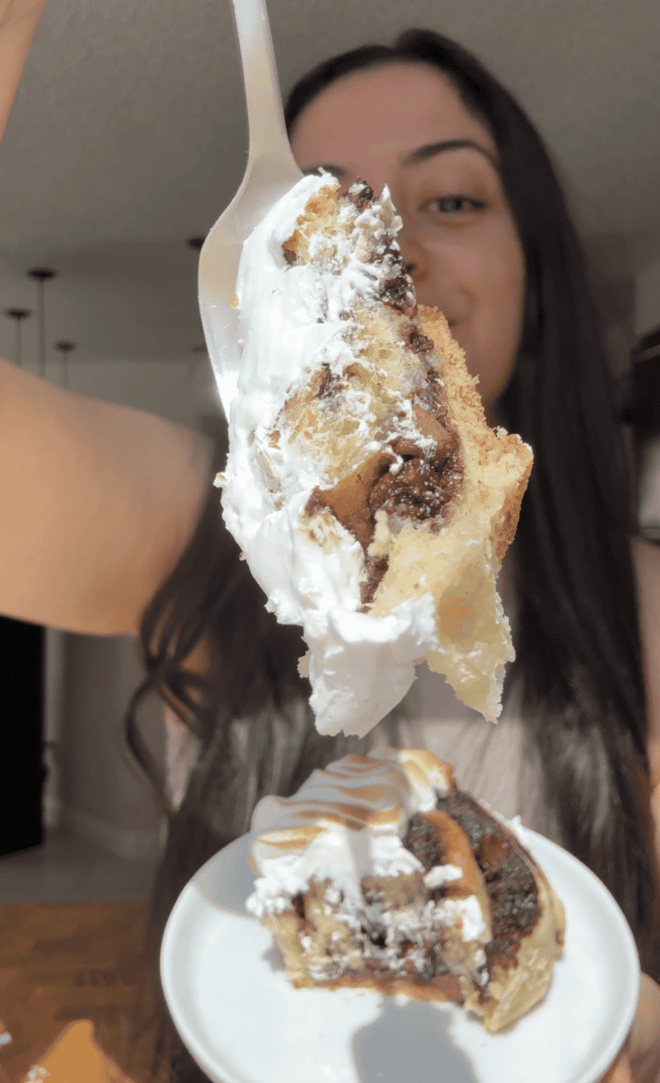 Forkful of a s'mores cinnamon roll with gooey chocolate and toasted meringue held over a plate