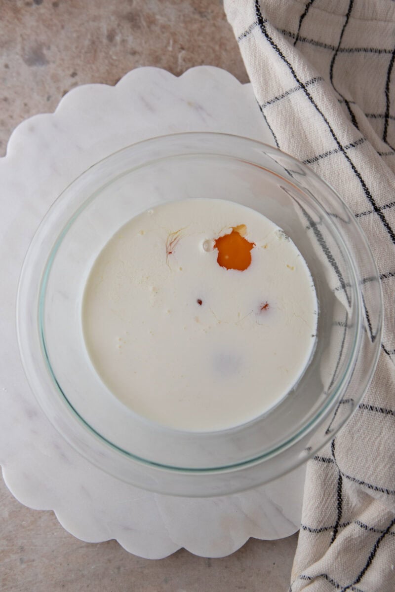 Egg yolks, whole egg, heavy cream and vanilla bean paste in a glass mixing bowl.