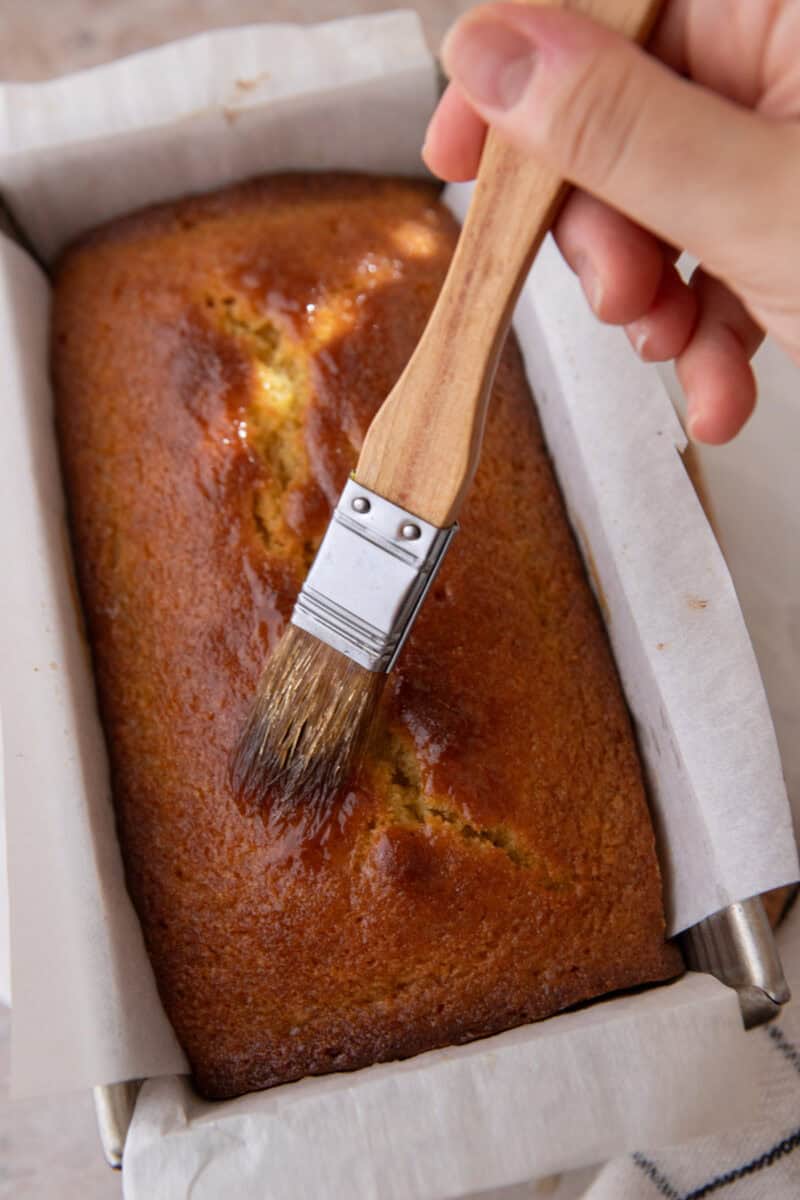 Warm honey syrup being brushed over the hot loaf so it soaks into the crumb.