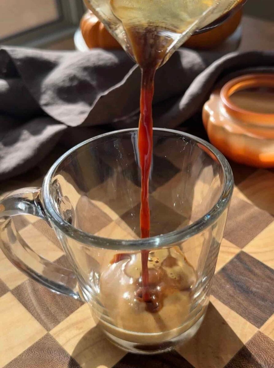 Hot espresso poured over two tablespoons of pumpkin spice sauce in a tall glass mug.