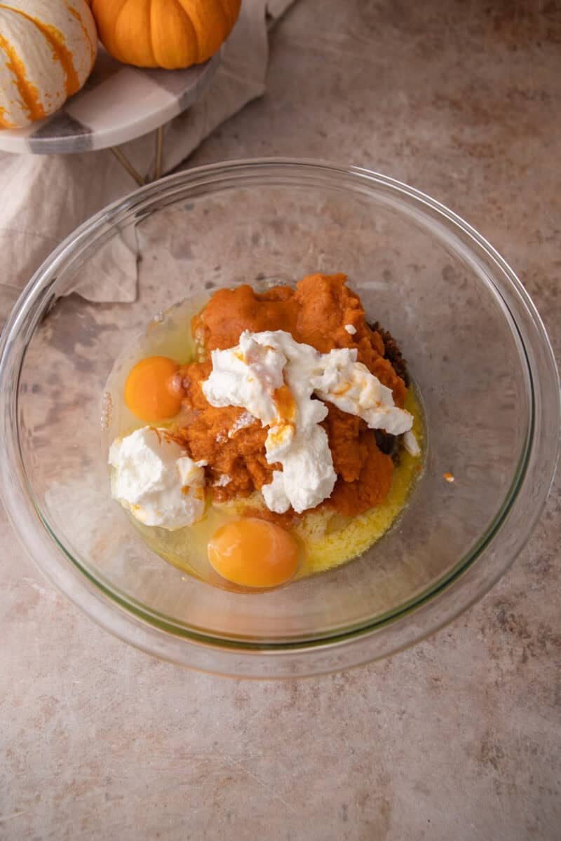 Pumpkin puree, eggs, Greek yogurt, and both sugars in a glass bowl before mixing.