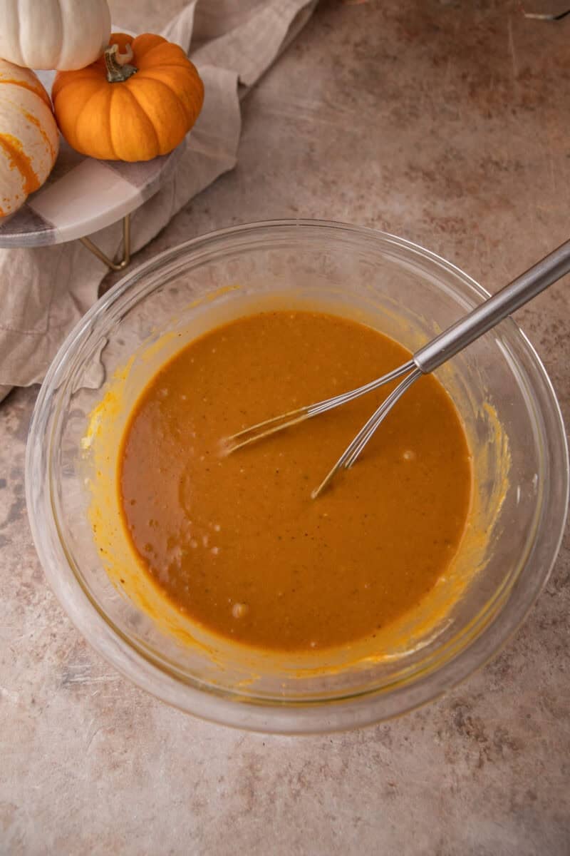 Smooth orange pumpkin muffin batter base whisked together in a large glass bowl.