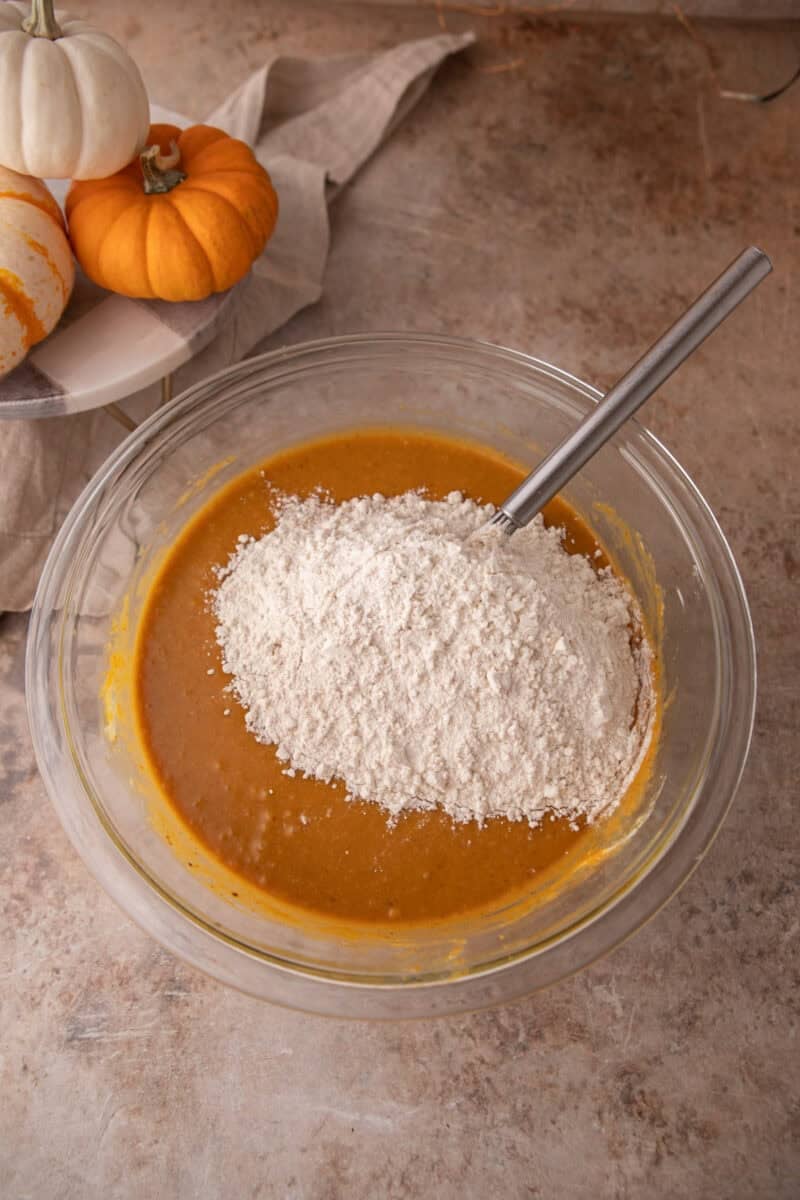 Flour, baking powder, baking soda, and salt tipped on top of the orange pumpkin mixture.