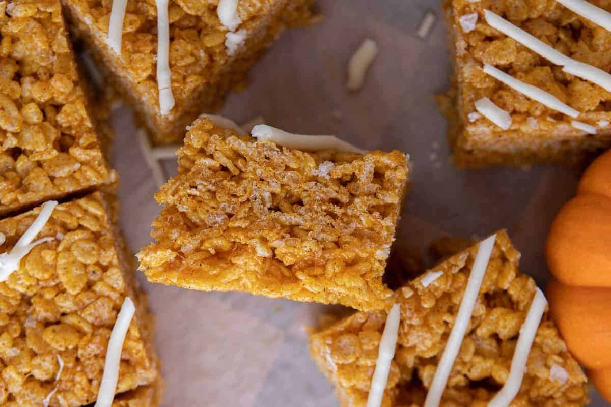 Square of pumpkin rice krispie treat topped with a white chocolate drizzle on parchment.