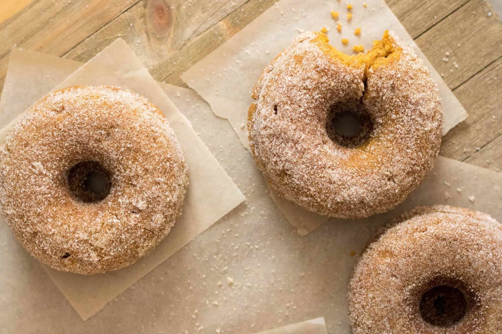 Finished small batch pumpkin donuts rolled in cinnamon sugar and stacked on parchment paper.