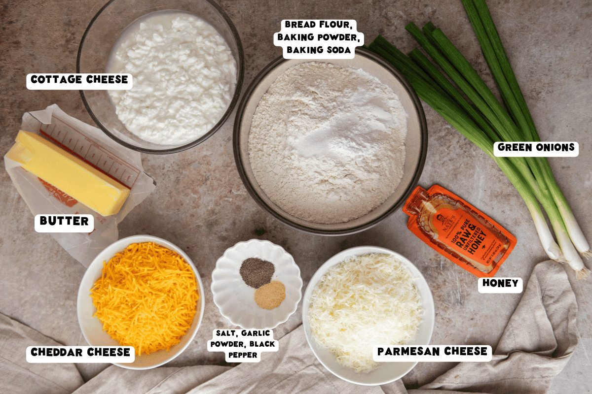 Labeled ingredients for cottage cheese biscuits, including cottage cheese, bread flour, butter, shredded cheddar, grated parmesan, green onions, honey, and seasonings.
