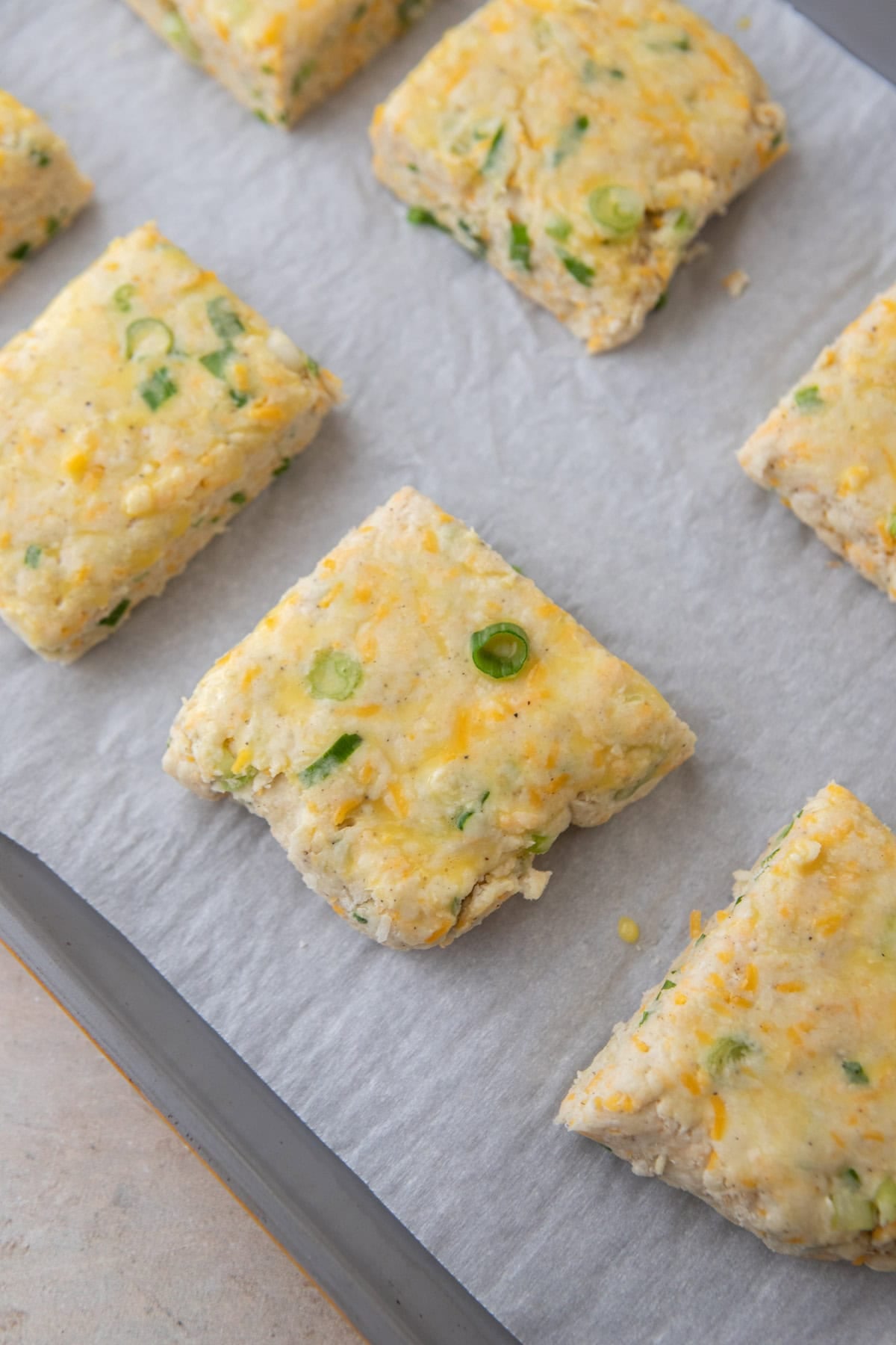 Unbaked biscuits brushed with egg wash on a parchment-lined baking sheet.