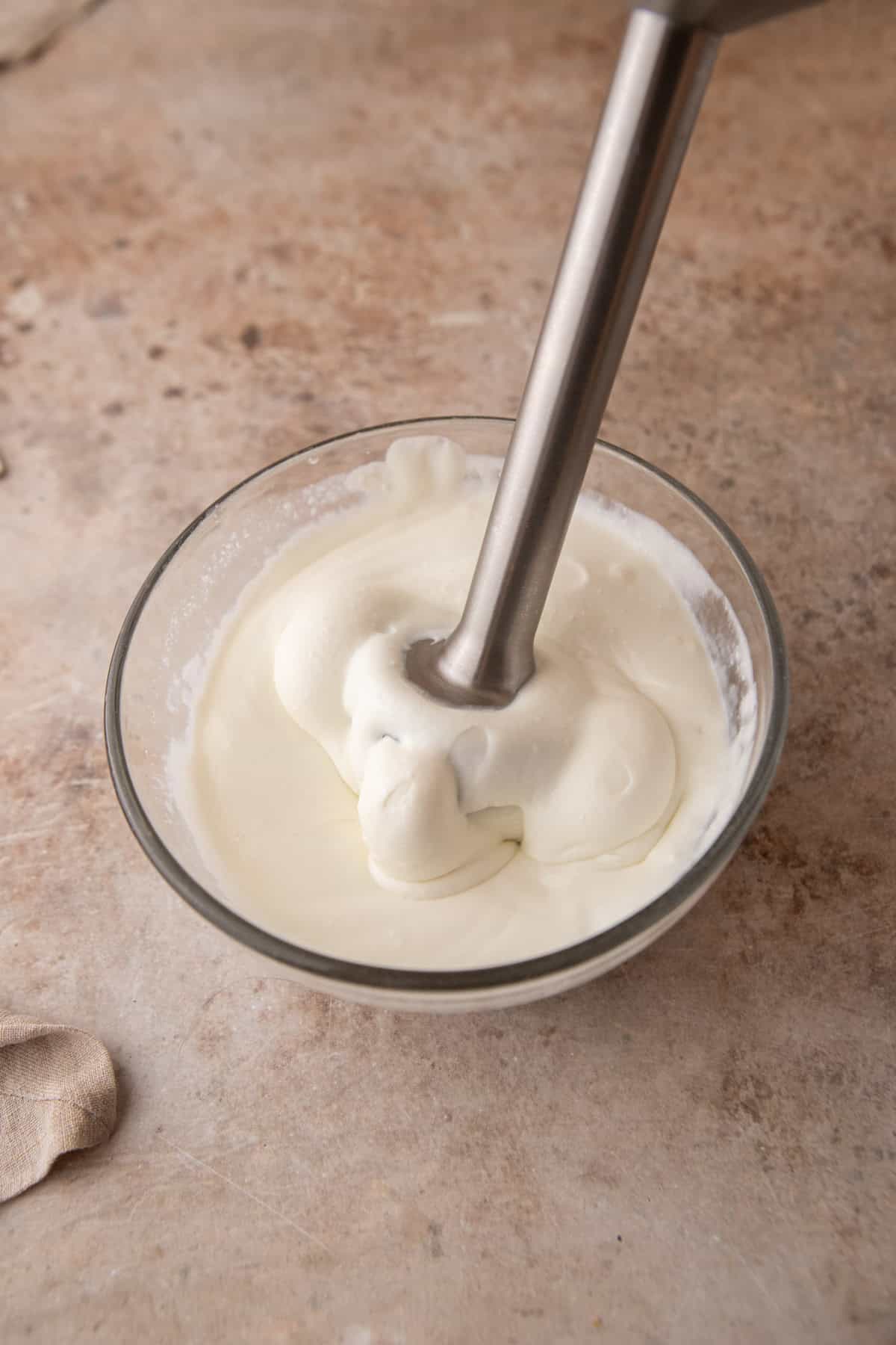 Immersion blender in a glass bowl of cottage cheese blended until smooth and creamy.