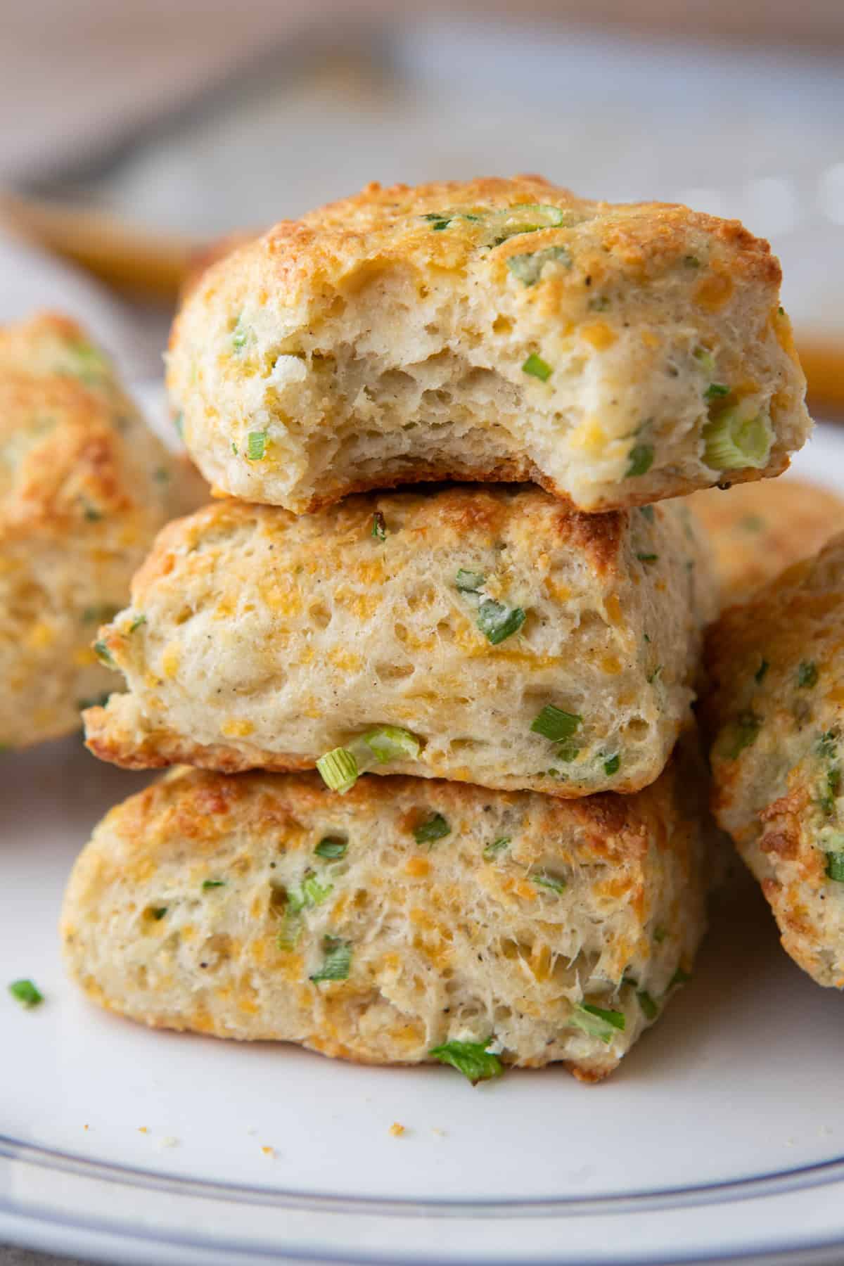 Stack of three cheddar green onion cottage cheese biscuits on a white plate, the top one with a bite taken out showing the soft, layered inside.