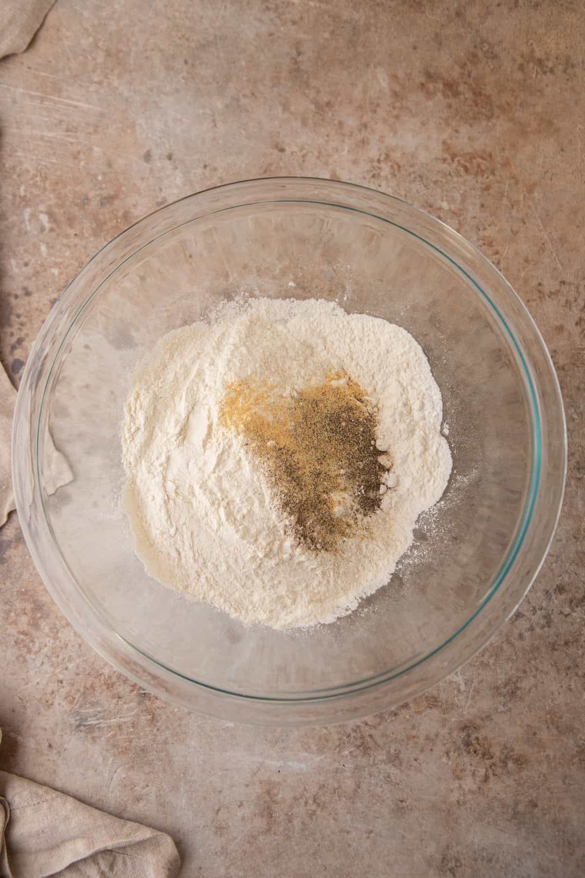 Bread flour, baking powder, salt, garlic powder, and black pepper in a glass mixing bowl.