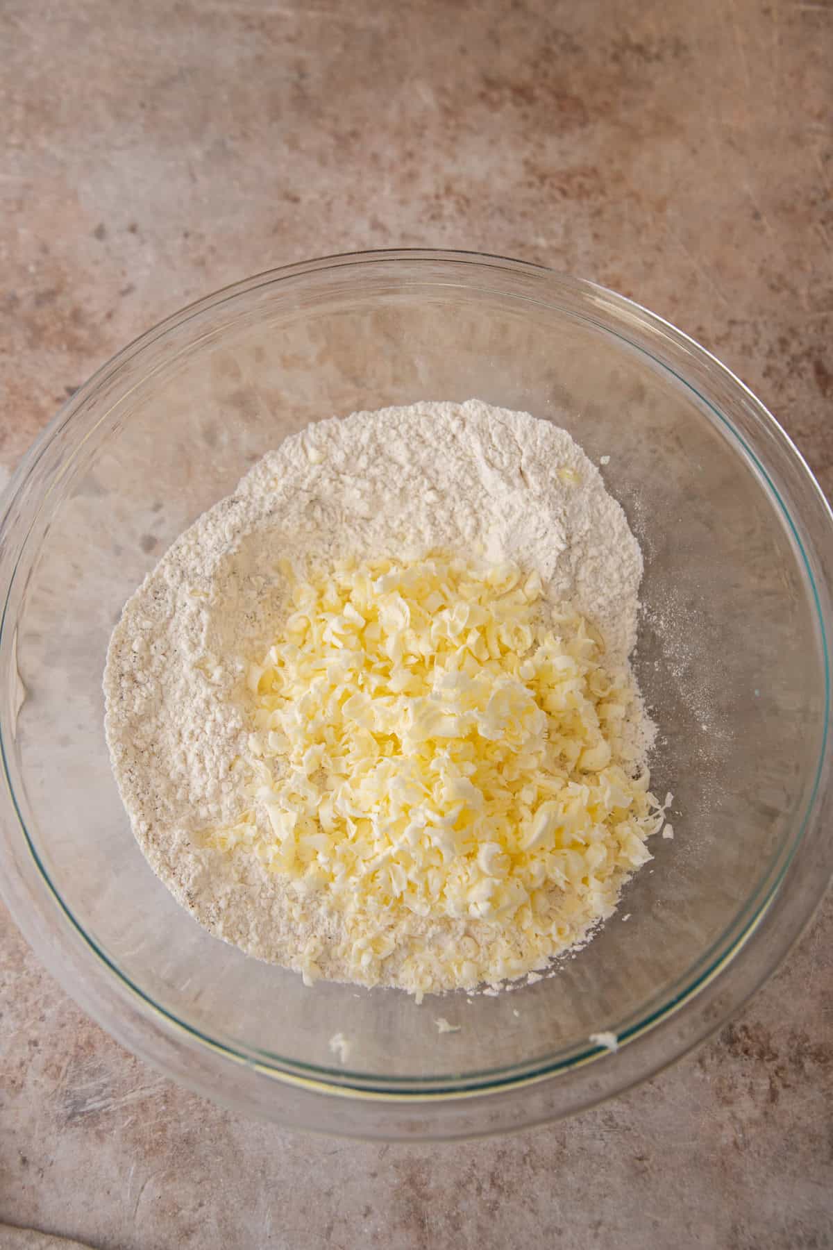 Grated frozen butter piled on top of the flour mixture in a glass bowl.