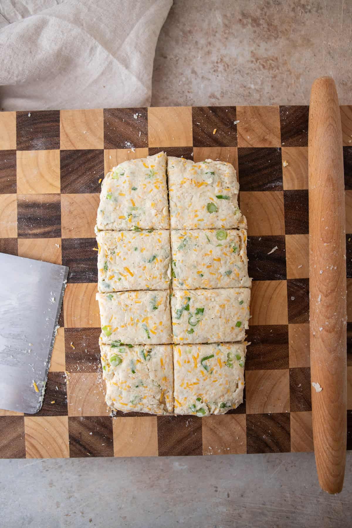 Rectangle of biscuit dough on a checkered cutting board next to a rolling pin.
